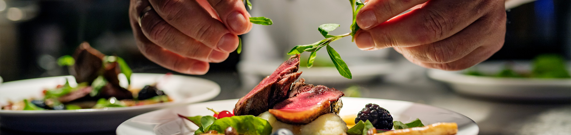 Feinschmeckergericht mit rosa gebratenem Fleisch, das von Hand mit frischen Kräutern angerichtet wird.