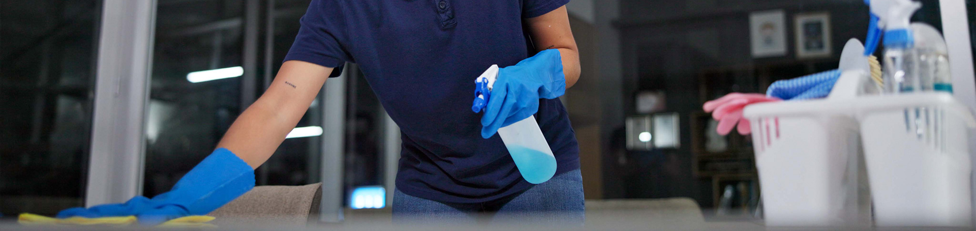 Reinigungskraft mit Handschuhen reinigt eine Oberfläche und verwendet eine Sprühflasche.